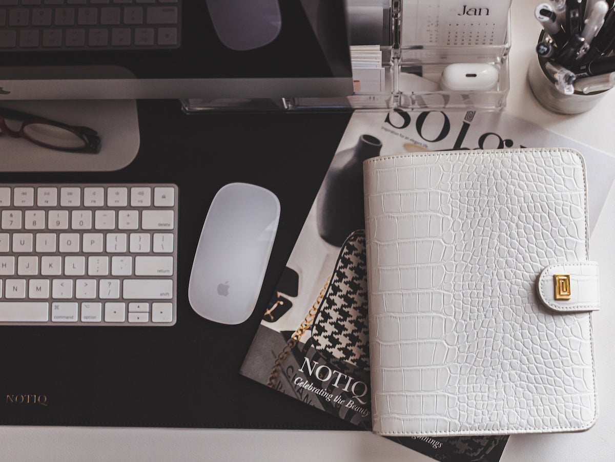 A white vegan leather croco planner laid closed on top a desk.
