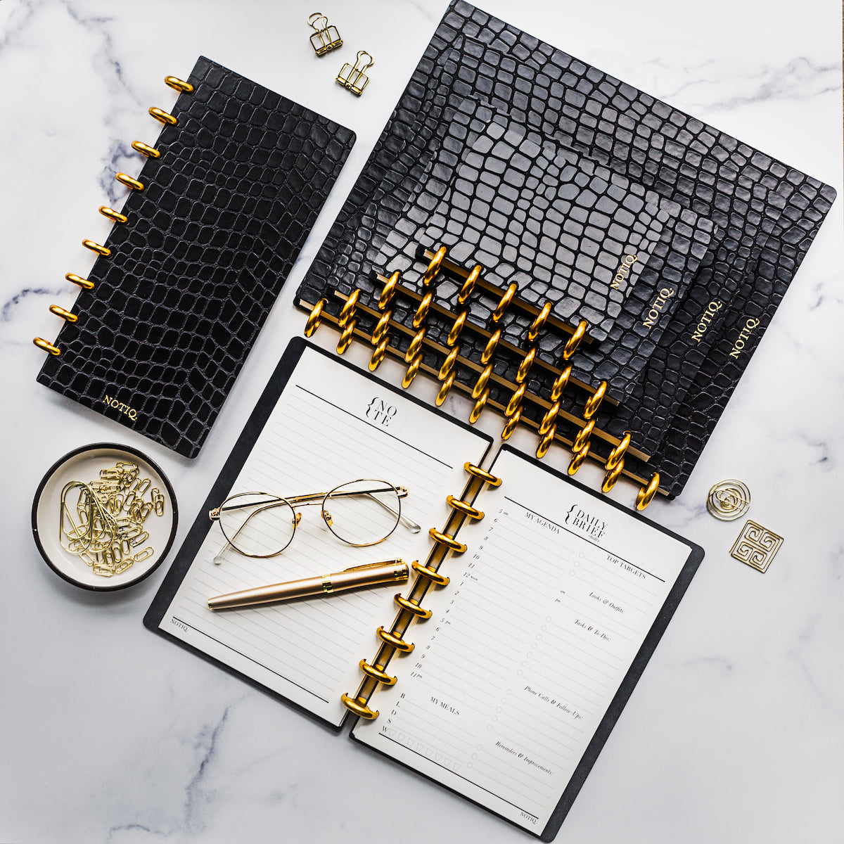 A stack of vegan leather black croco planner notebooks in various sizes.