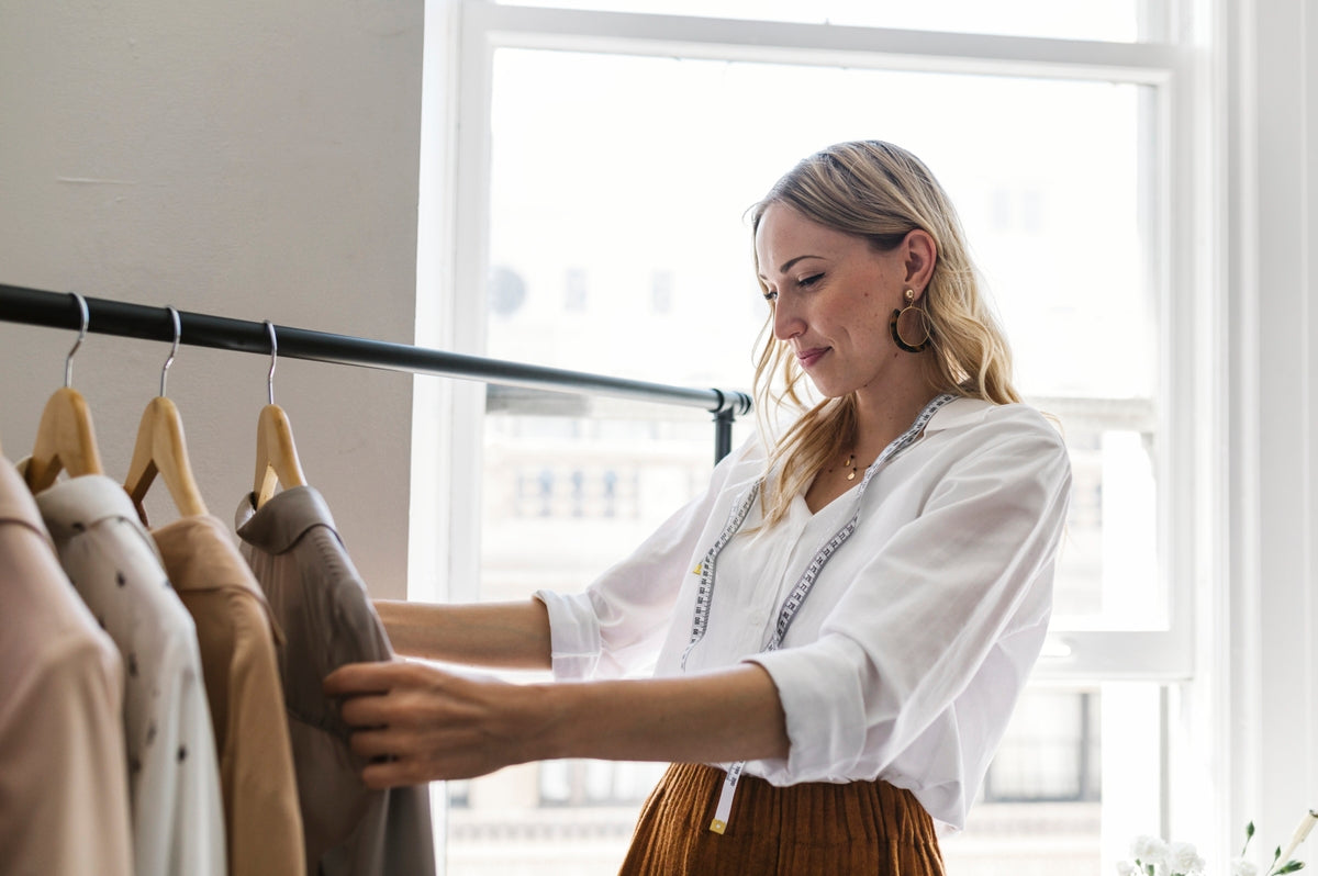 A young female designer admiring clothes on a clothing rack.