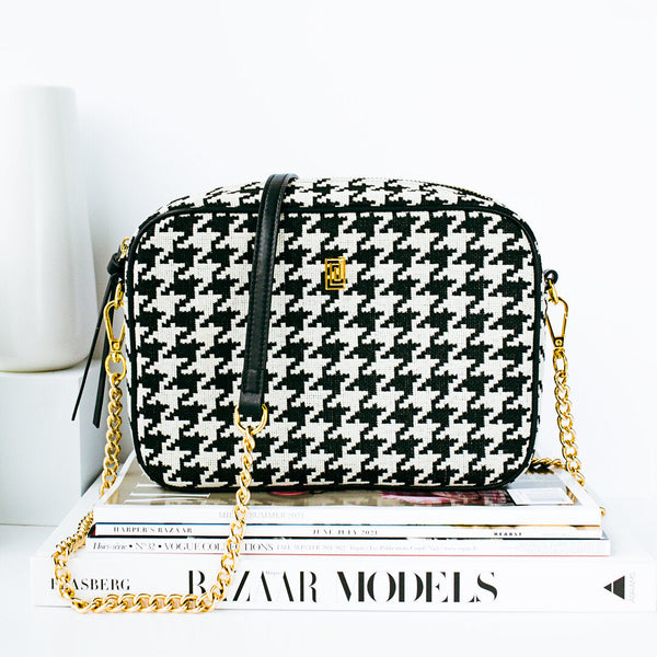 Luxury black and white houndstooth crossbody chain bag on stack of books.